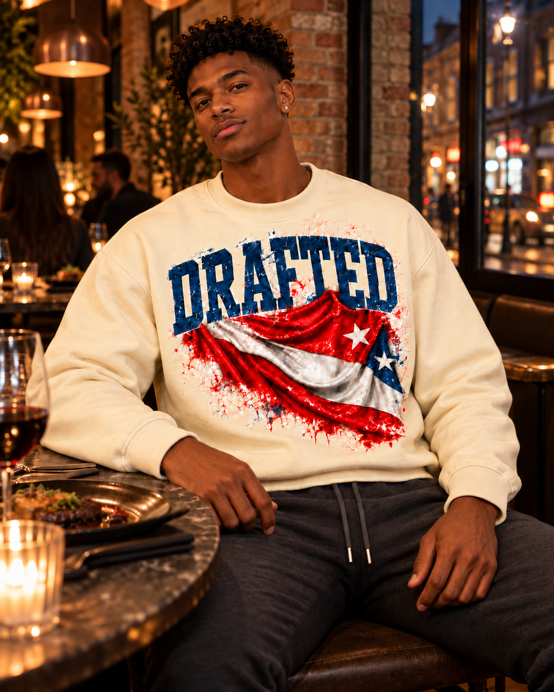 Young adult AI male model wearing the cream Drafted flag sweatshirt and charcoal joggers at dinner in East London