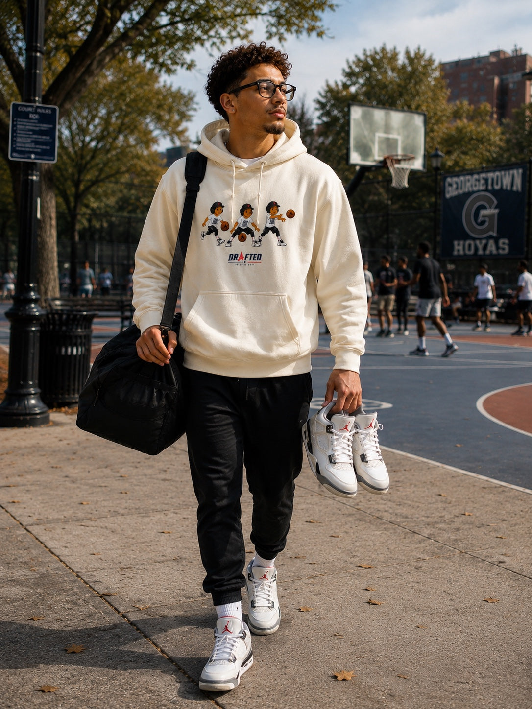 Model wearing the cream Triple Threat Cartoon Hoodie beside a basketball court